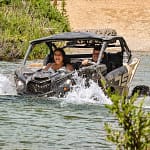 bride and groom cross a river in an ATV